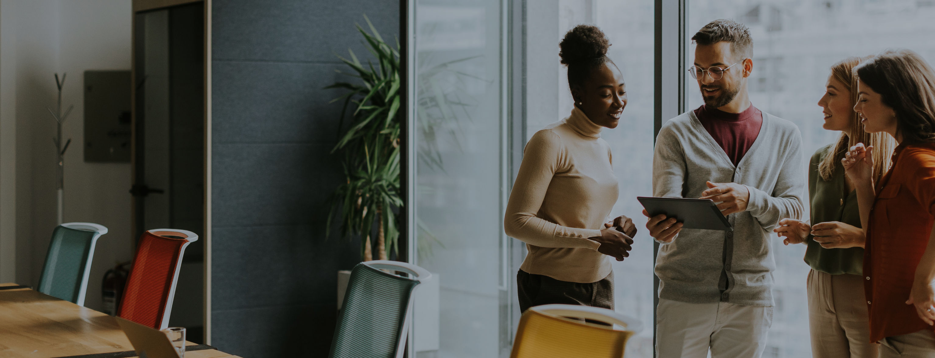 Four people in a boardroom, one holding a tablet and pointing at the screen