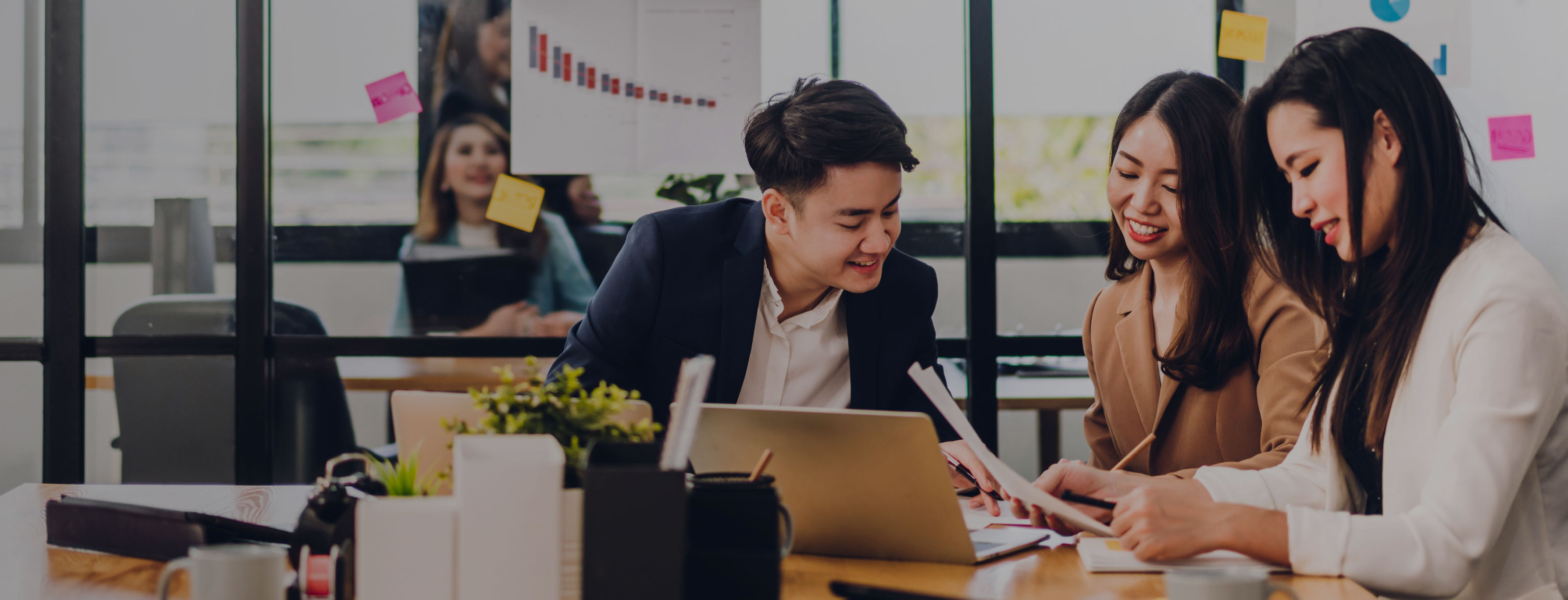 Three people sitting smiling and looking at a laptop and a notepad