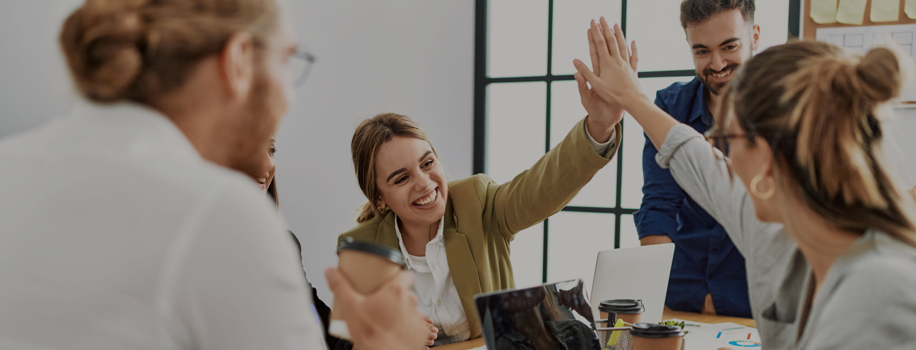 Two women smiling and high-fiving while sitting, watched by others