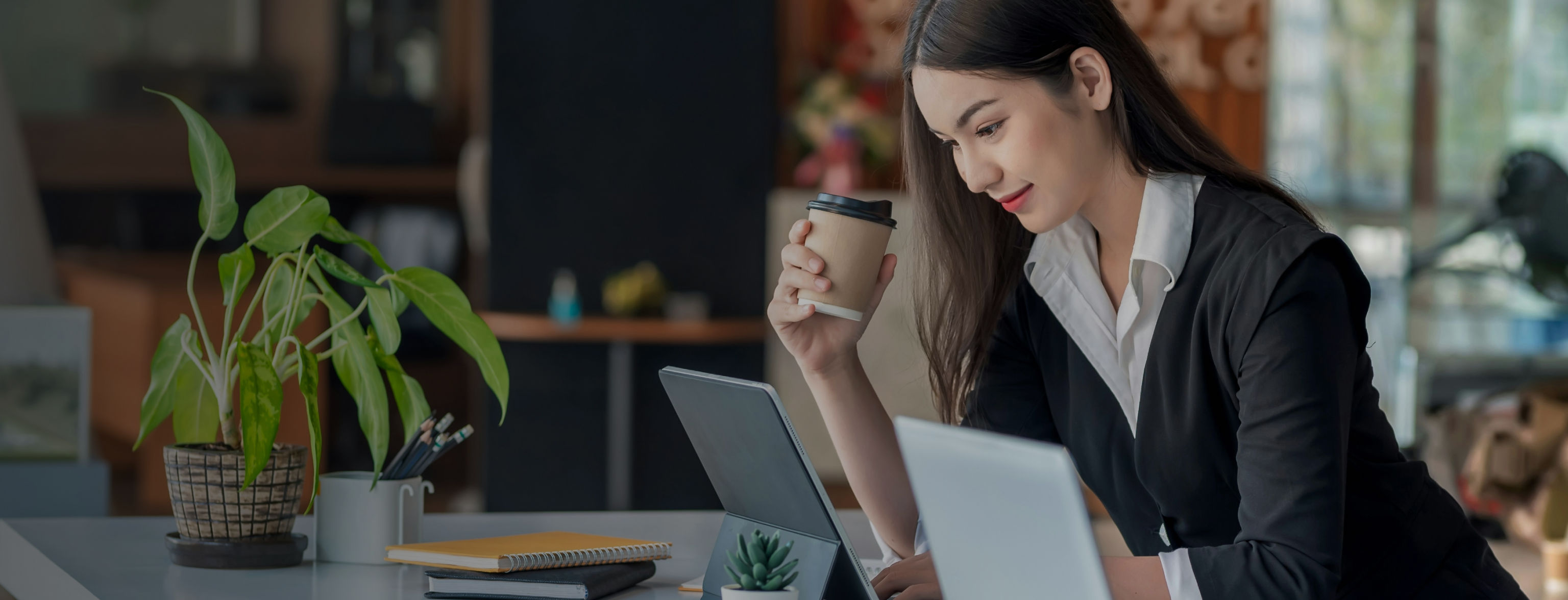 A standing woman looking over a laptop with a coffee cup in her hand