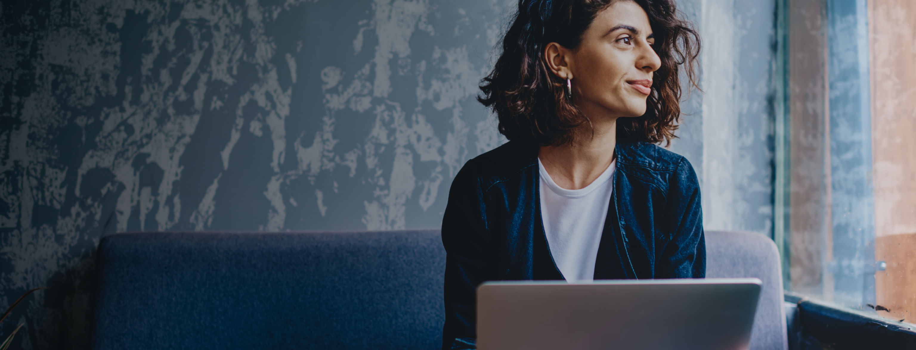 A woman with a laptop in front of her sitting looking out the window