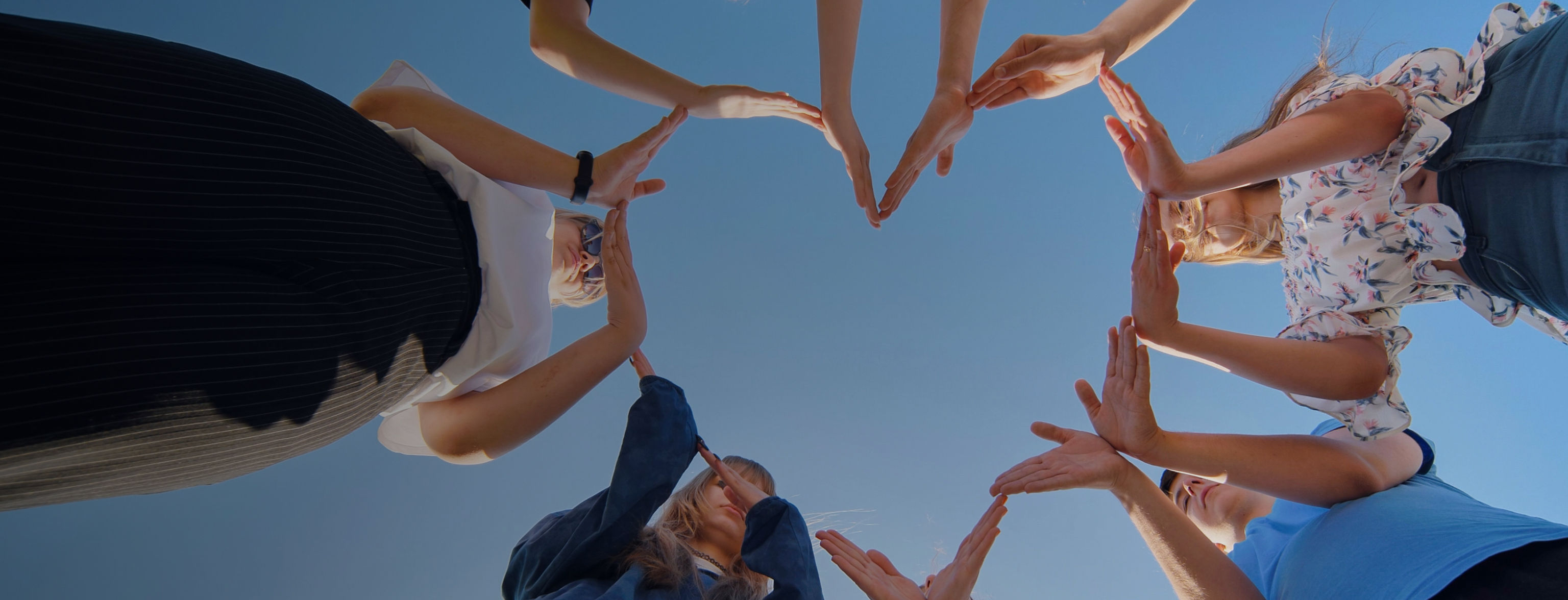A group of people using their hands to make a heart shape, the image taken from the ground upwards