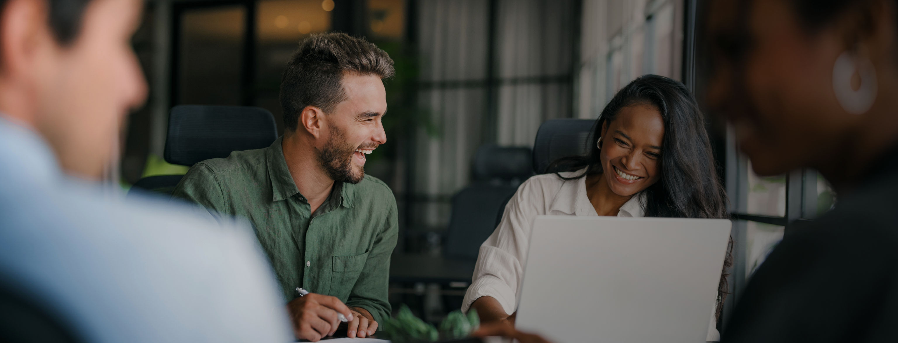A man laughing towards a smiling woman who is looking at a laptop