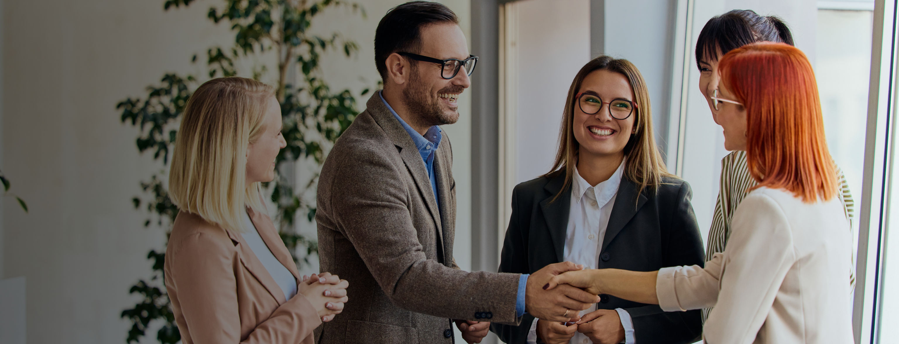 A group of smiling people watching a smiling man and woman shake hands