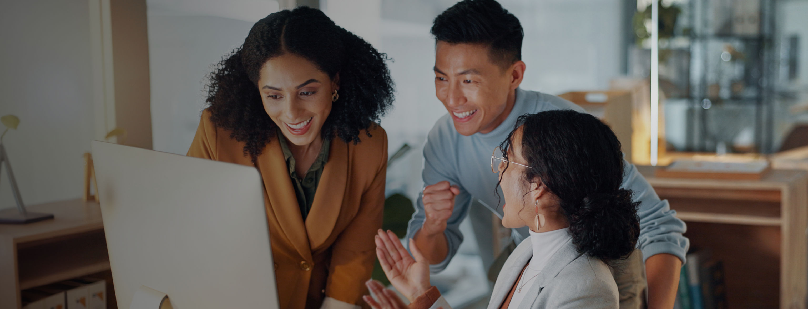 Three people, two standing, one sitting, celebrating results on a computer monitor