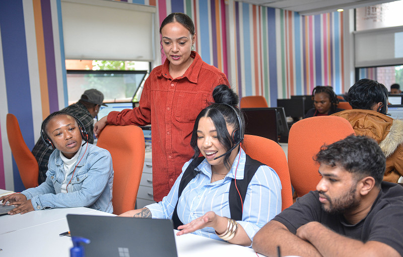 Three people sitting and one person standing, looking at a laptop screen