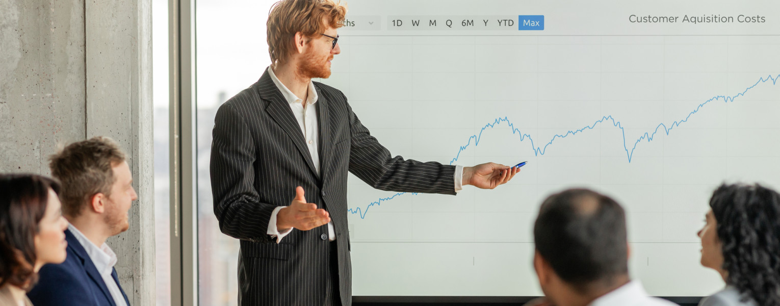 A man presenting to four others, showing a line chart going up over time