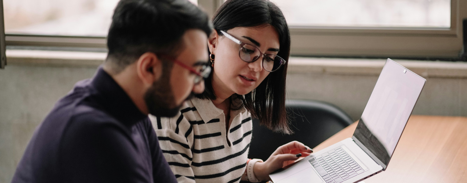 A man and a woman looking at a laptop screen and phone
