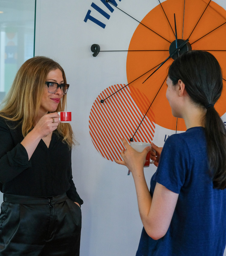 Two women standing with coffee cups, in front of a whiteboard