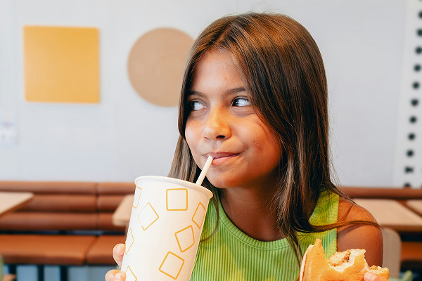 A girl drinking from a plastic cup a burger in her other hand