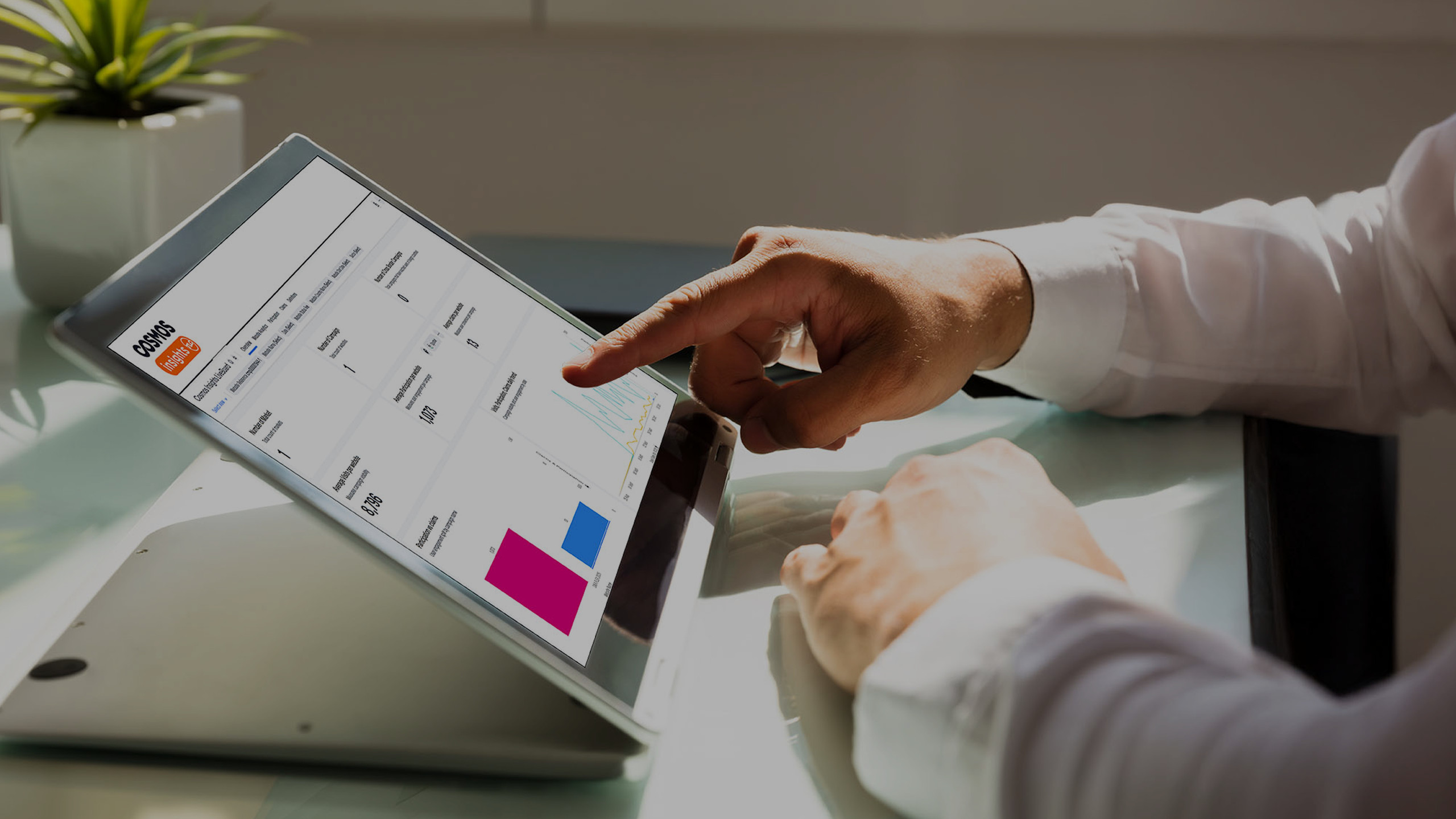 A tablet screen showing the Cosmos platform with a finger pointing to the screen