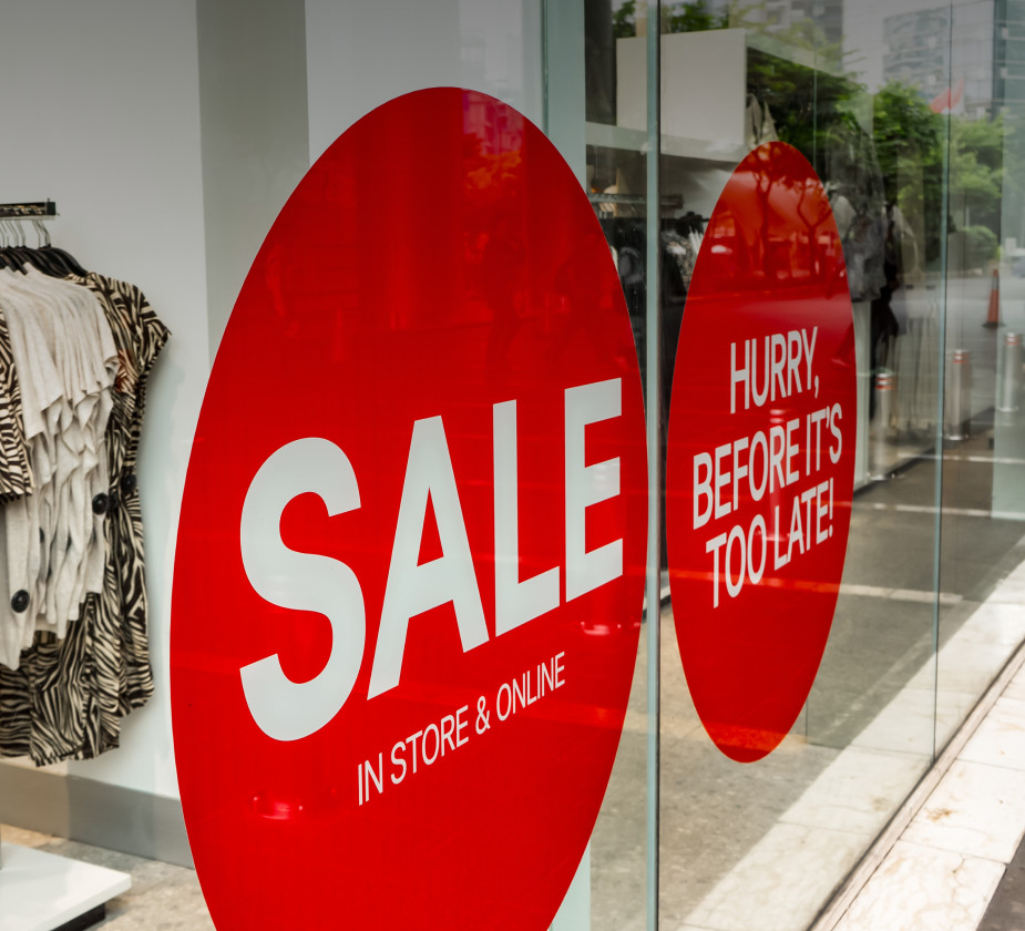 A red sale sign in a store window reads "SALE IN STORE &amp; ONLINE" with "HURRY, BEFORE IT'S TOO LATE!" and clothing in the background.