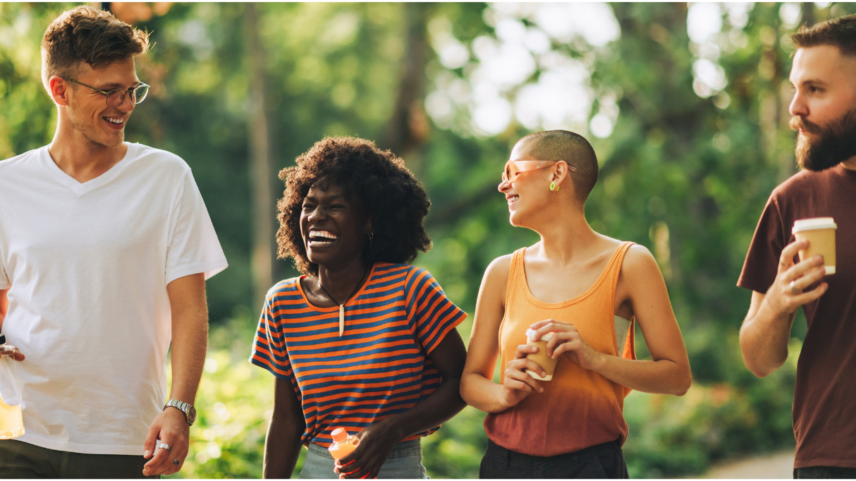 A group of four friends walking together outdoors, smiling and enjoying each other's company.