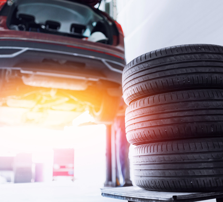 A car is lifted on a hydraulic lift, and a stack of four tires is in the foreground