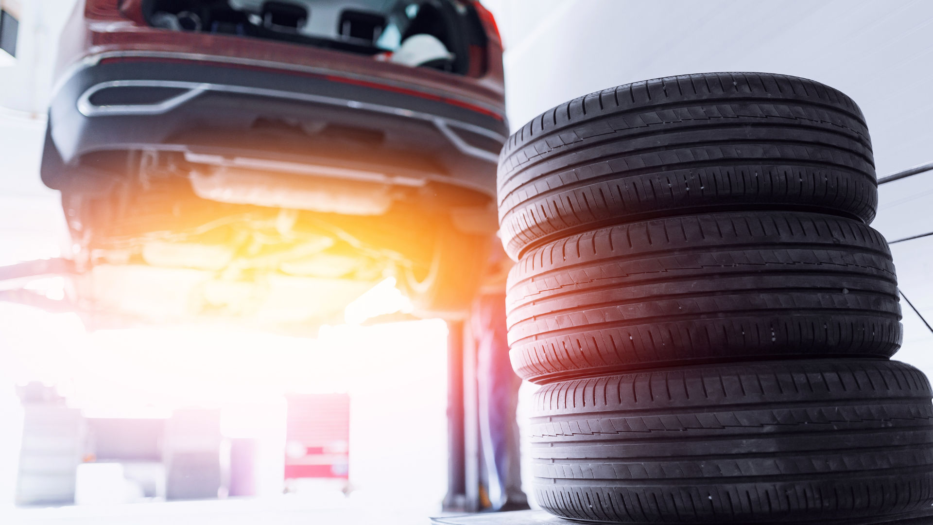 A car is lifted on a hydraulic lift, and a stack of four tires is in the foreground