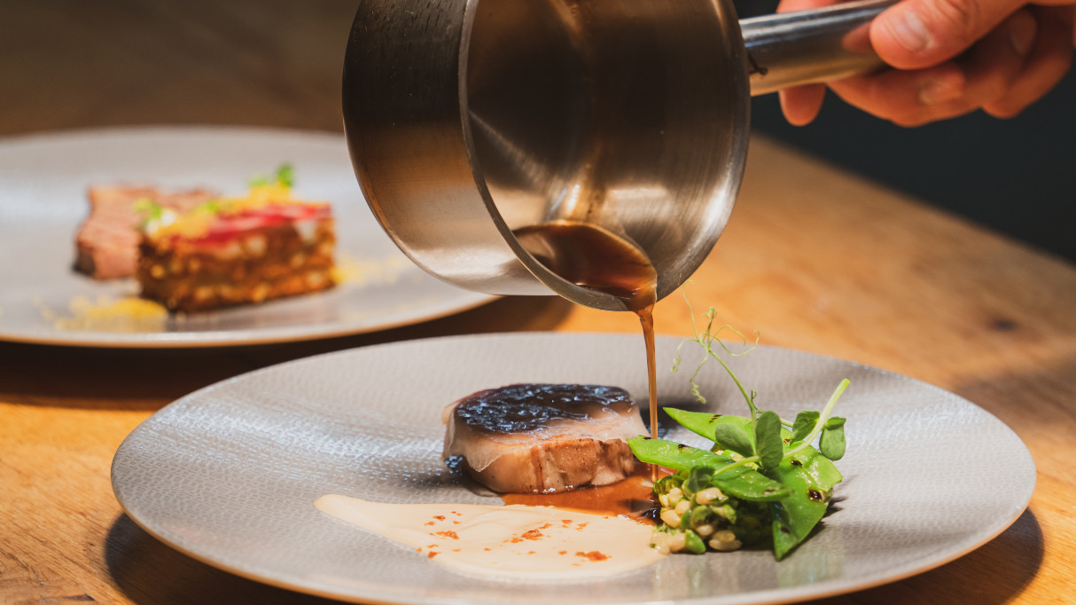 A plate of food with a piece of meat, sauce being poured over it