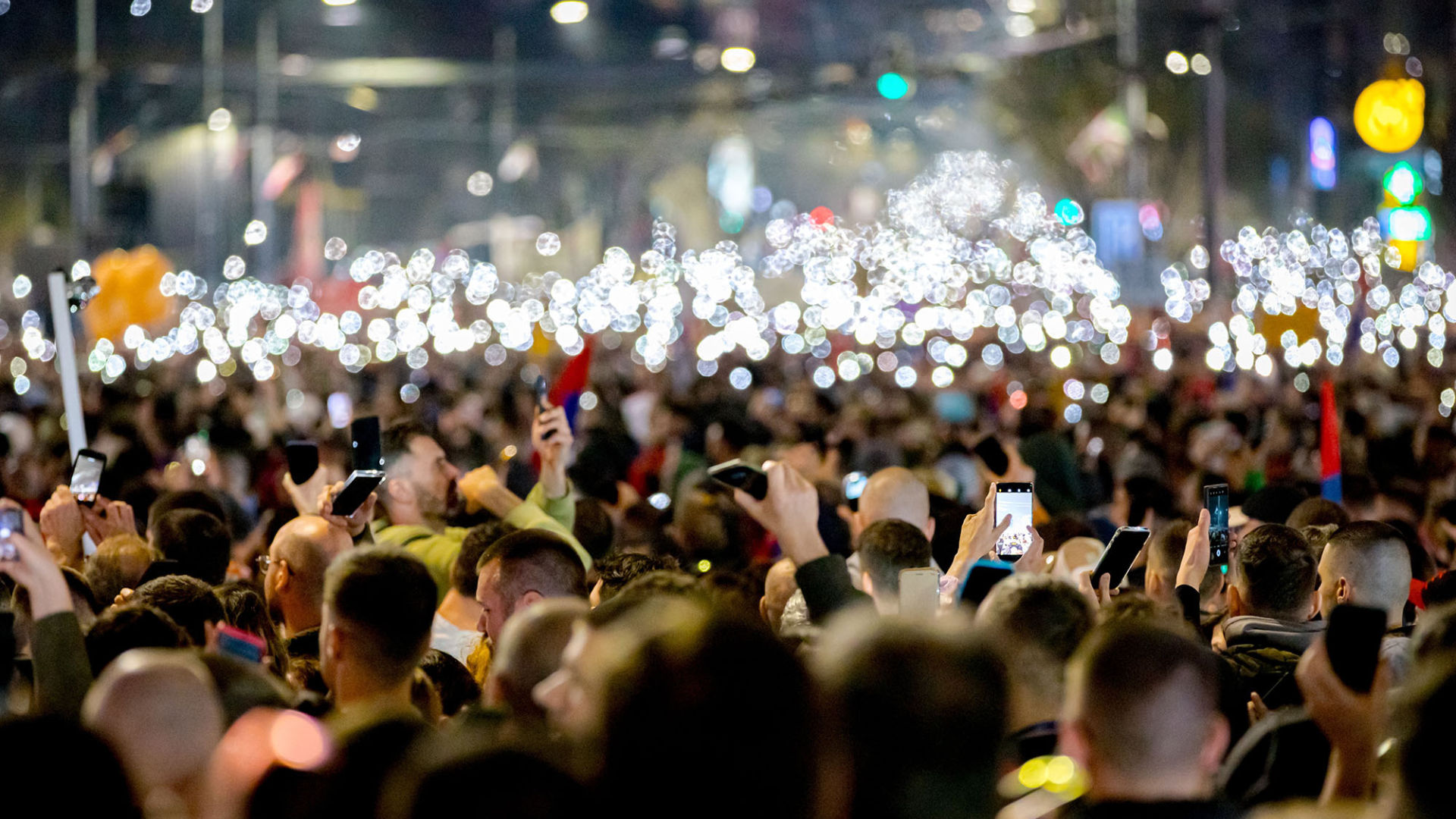 Crowd holding up phones with lights on in a nighttime setting.