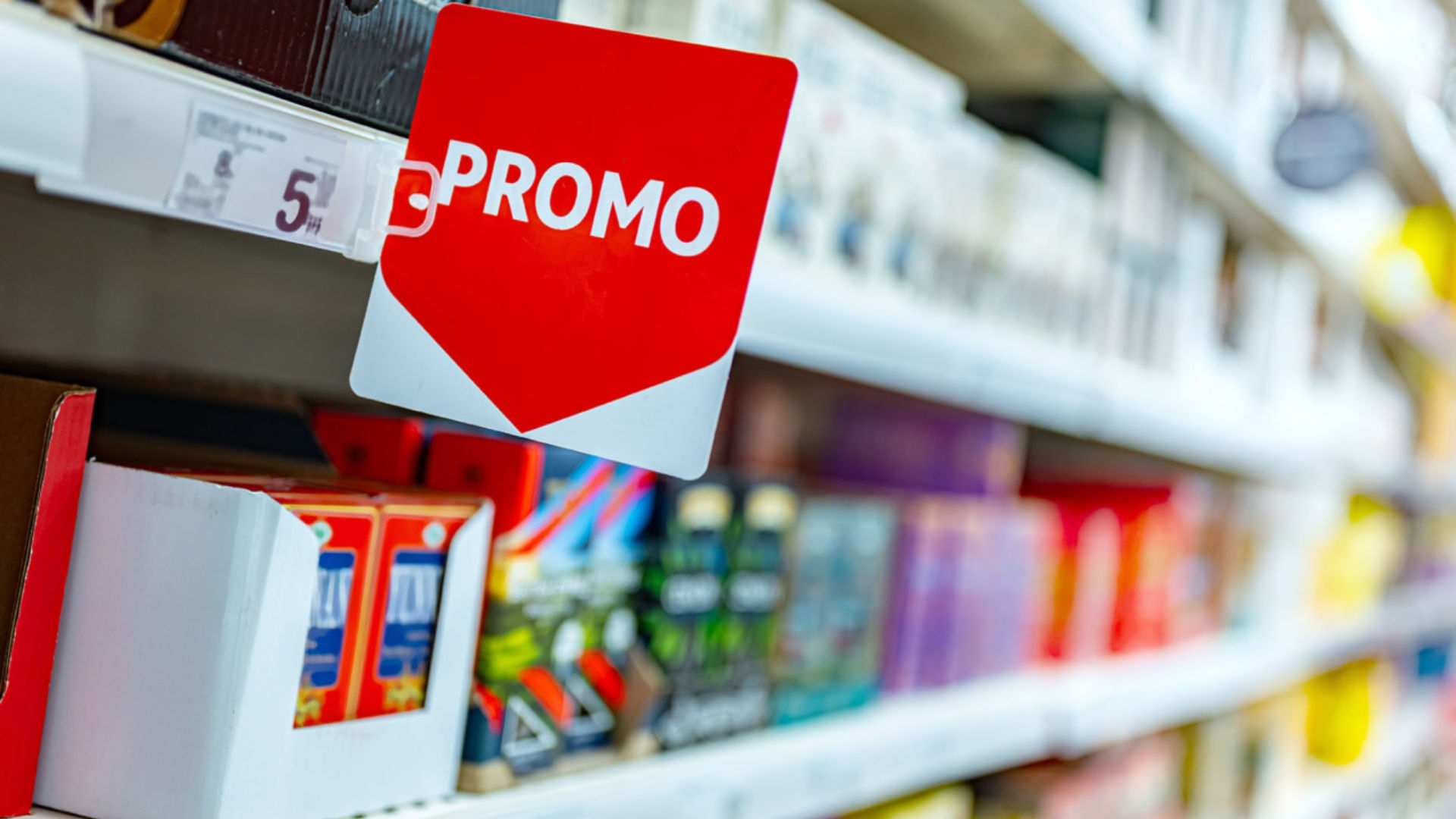 A promotional sign in a store aisle, indicating discounts on products displayed on shelves.
