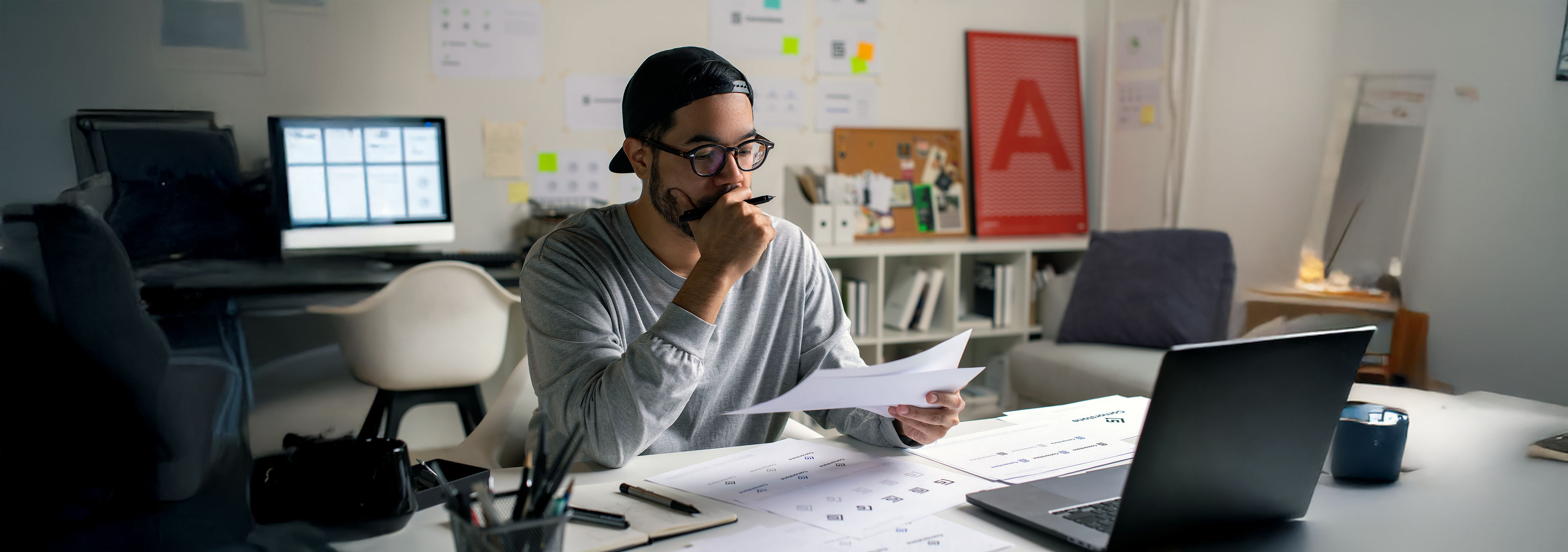 man sitting at laptop working on a computer but he looking at paper and thinking