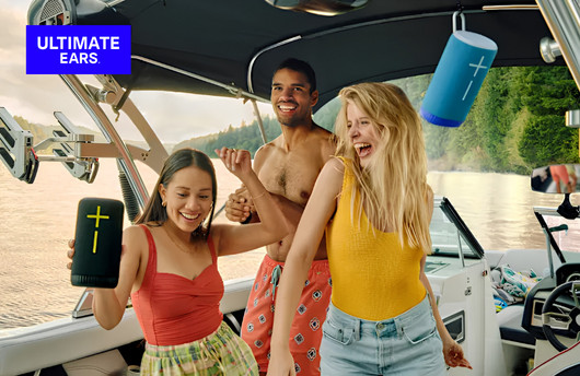 Three people enjoying music outdoors on a boat while holding Logitech Ultimate Ears portable speakers.