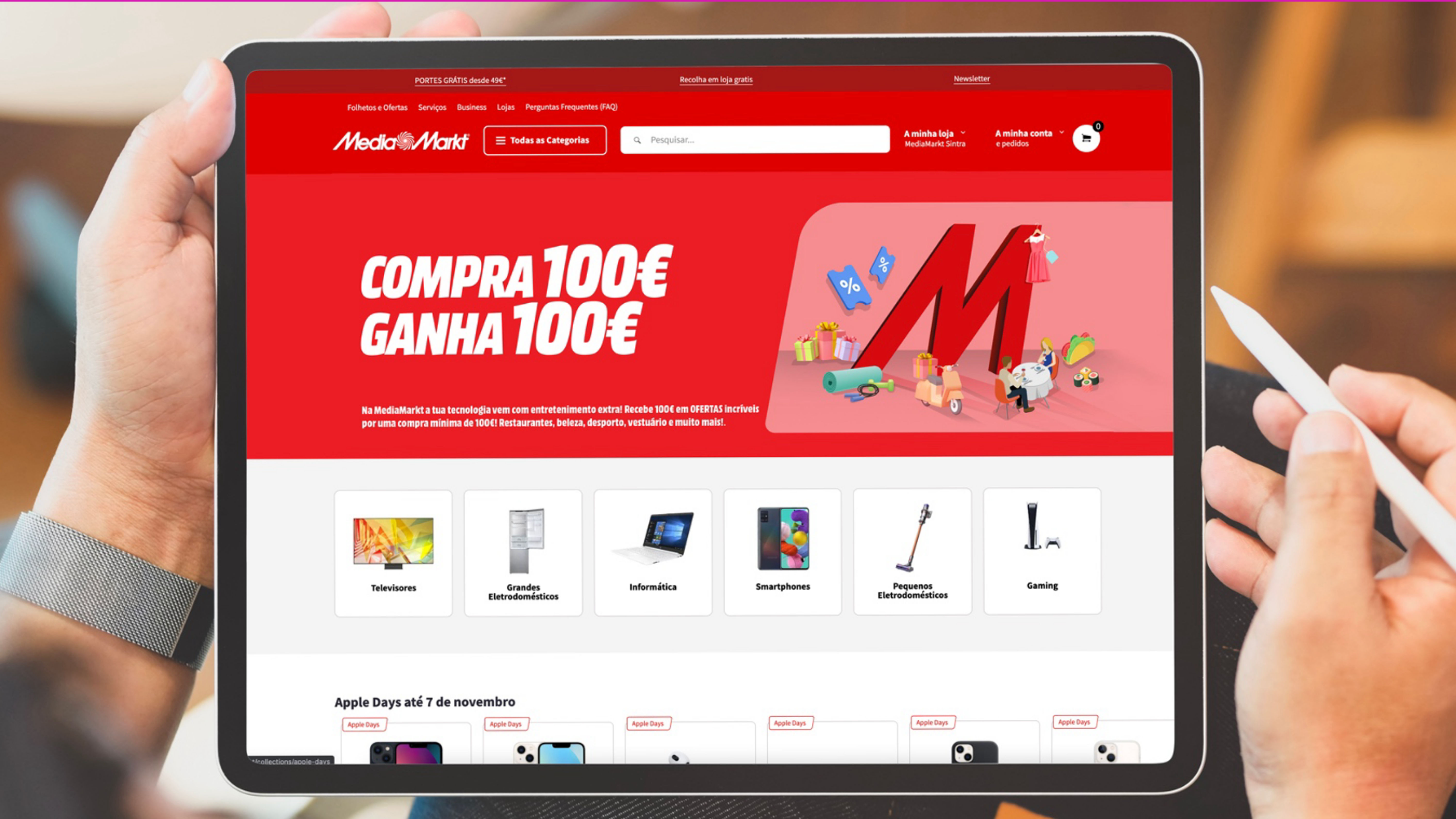 Tablet displaying a MediaMarkt website with a red banner saying "Compra 100€ Ganha 100€."