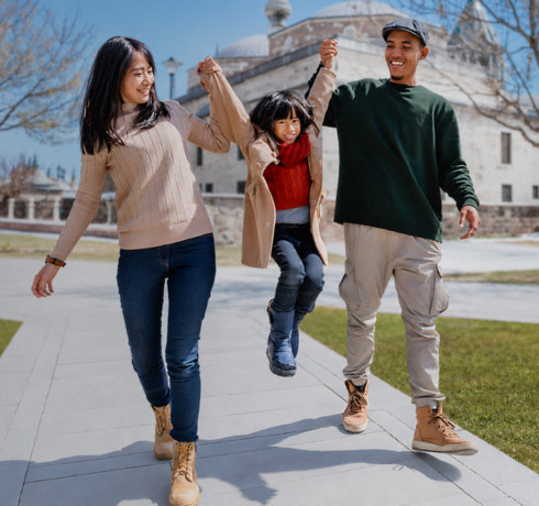 A woman and a man are playfully holding up a girl between them while walking outdoors