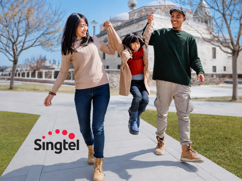 A woman and a man are playfully holding up a girl between them while walking outdoors