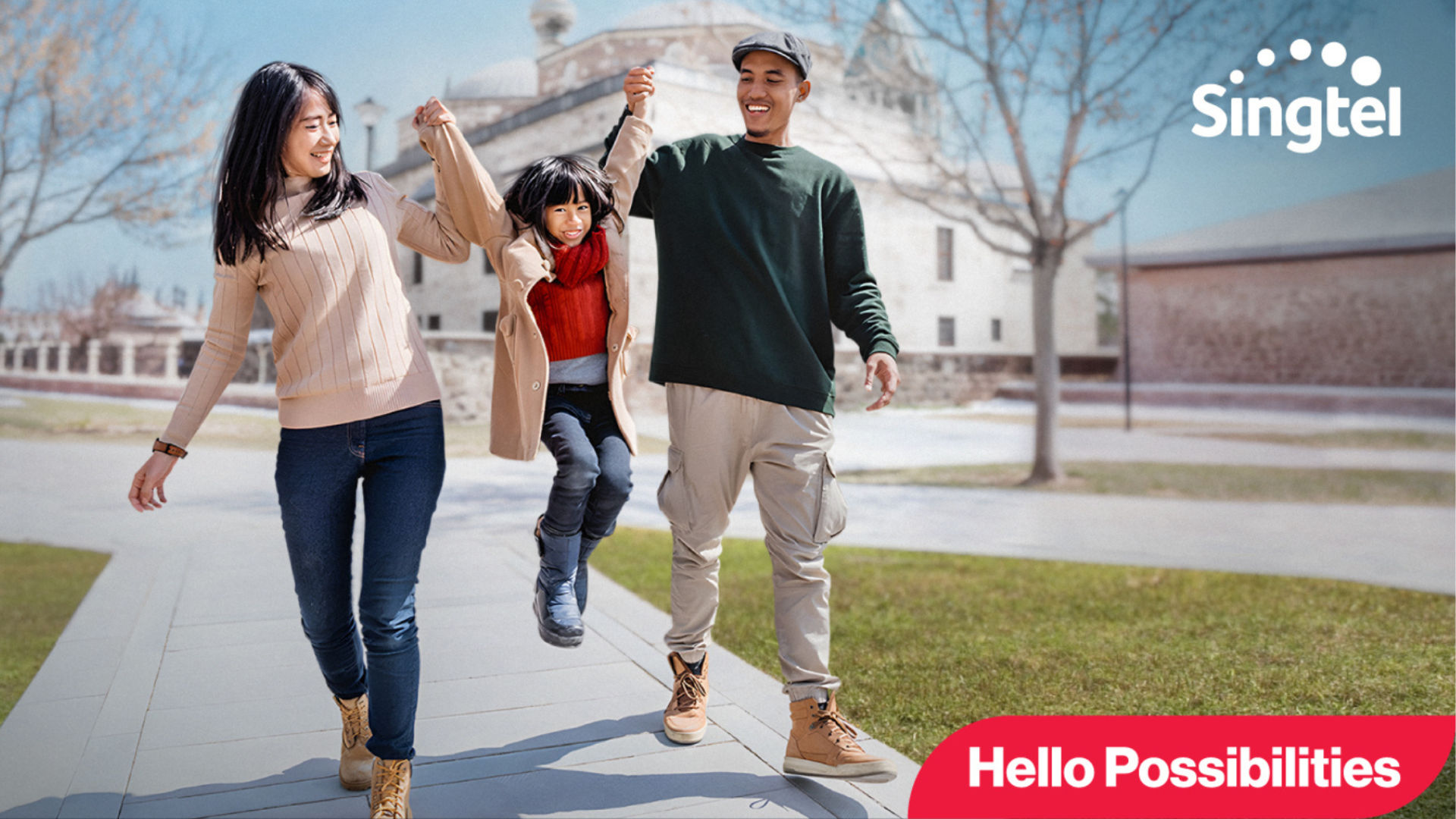 A woman and a man are playfully holding up a girl between them while walking outdoors