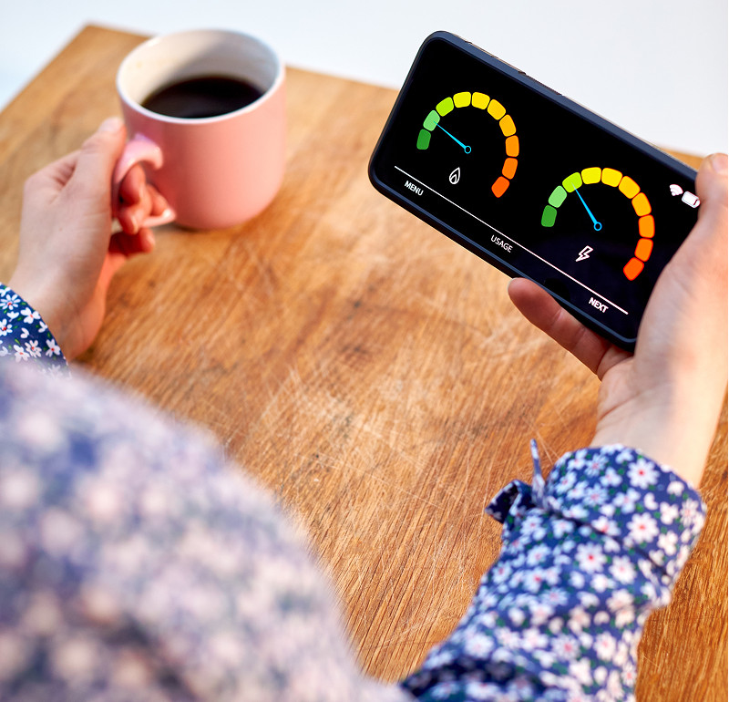 A woman holding a smart meter in one hand and a cup of coffee in the other