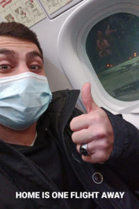 Selfie of myself with a mask on sitting in the emergency exit row of the airplane.
