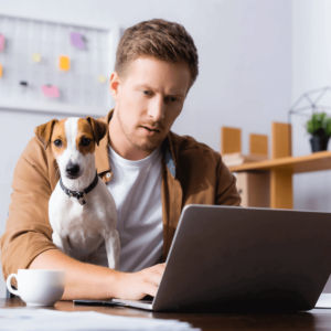 Mann mit einem Hund sitzend am Büro mit Laptop