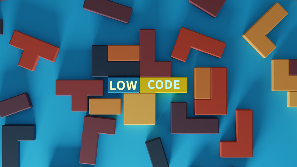 Eine Ansammlung von Bauklötzen, die an Tetris-Klötze erinnern, liegt auf einem blauen Tisch. In der Mitte des Bildes steht das Wort "Low Code" geschrieben.