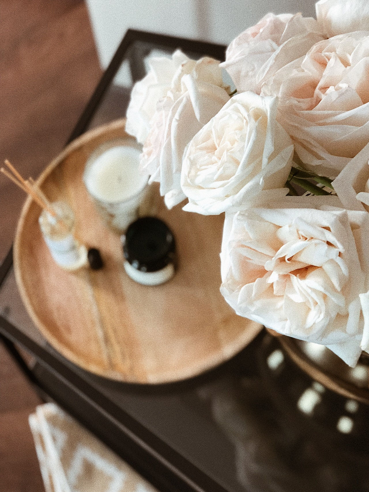 Blush roses, a lit candle, and incense arranged on a wooden tray.