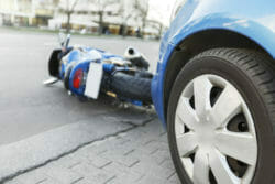 The accident blue bike with a blue car. The motorcycle crashed into the bumper of the car on the road. The motorcycle lies on the road near the car.