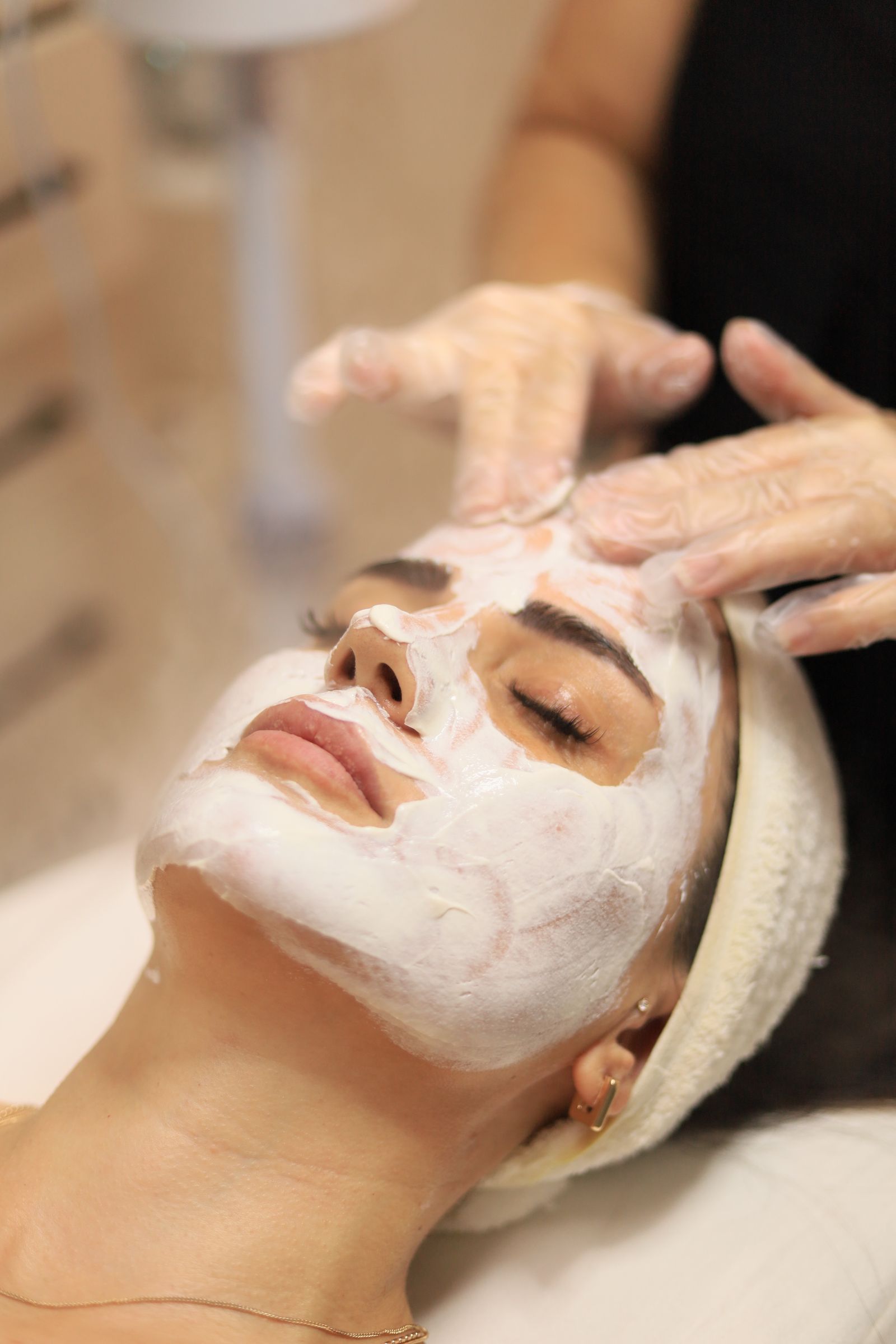 An aesthetician working a treatment mask across a client's face in gloved hands