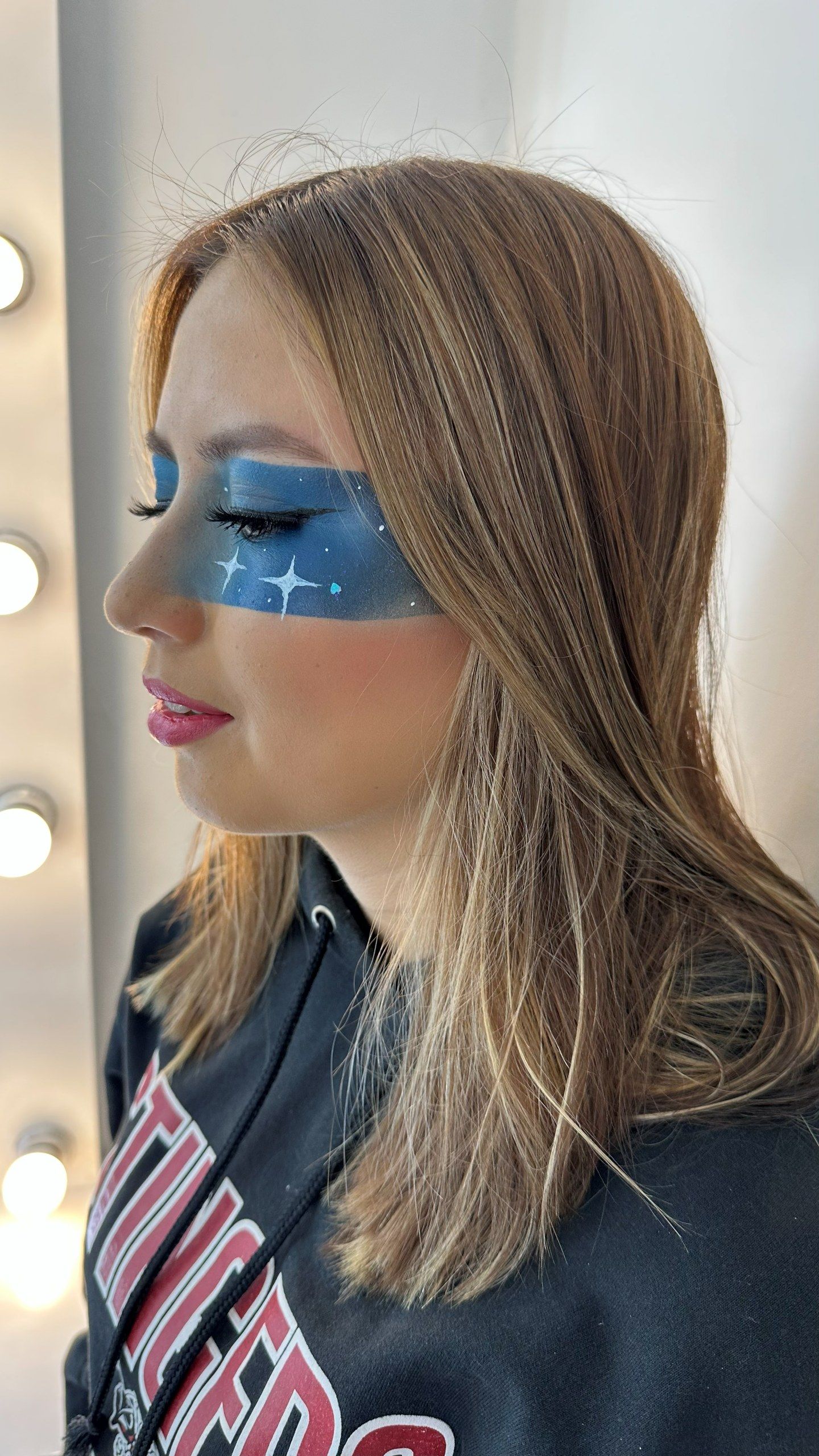 Maquillaje gráfico de perfil: una franja azul intensa sobre los ojos con estrellitas blancas y labios rosa