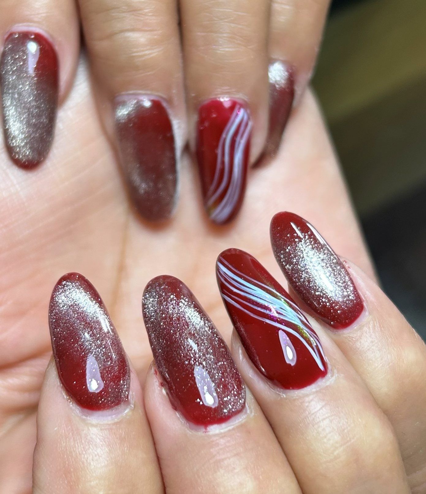 Uñas almendradas largas en chrome cat-eye borgoña, con la luz marcando una banda en cada uña