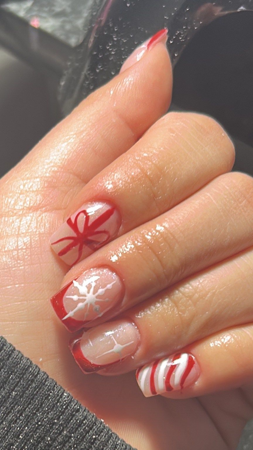 Uñas cortas con francesa roja, un moño de regalo pintado a mano, un copo de nieve y una raya de bastón de caramelo