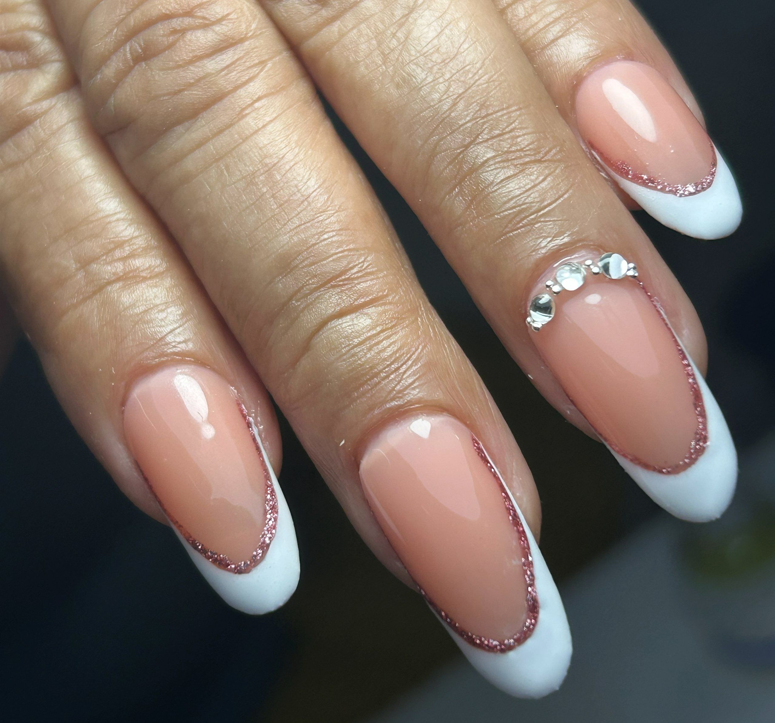 Uñas almendradas con francesa blanca, una línea fina de glitter sobre la sonrisa y un grupo de cristales en el anular