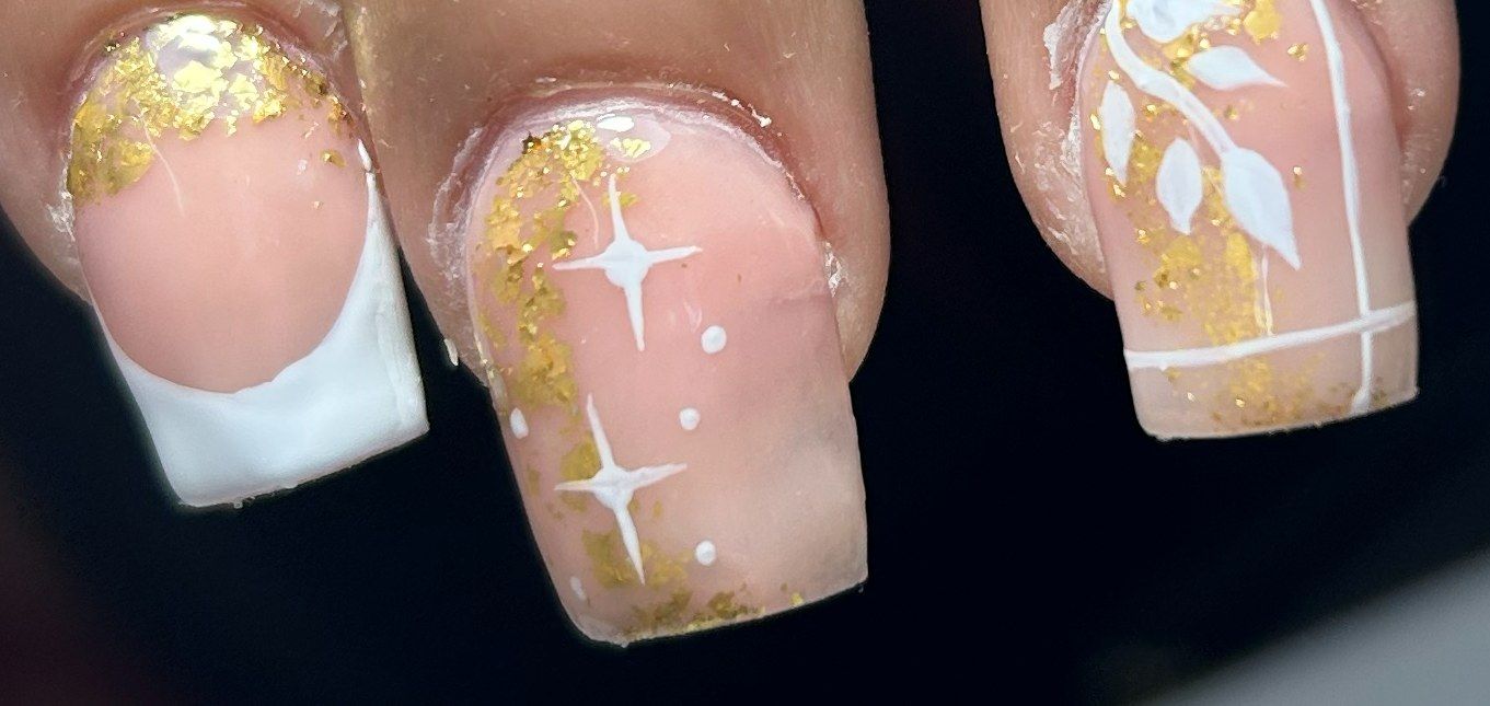 Primer plano de uñas cuadradas con hojuelas doradas, francesa blanca, estrellas blancas pintadas a mano y un diseño de hojas blancas