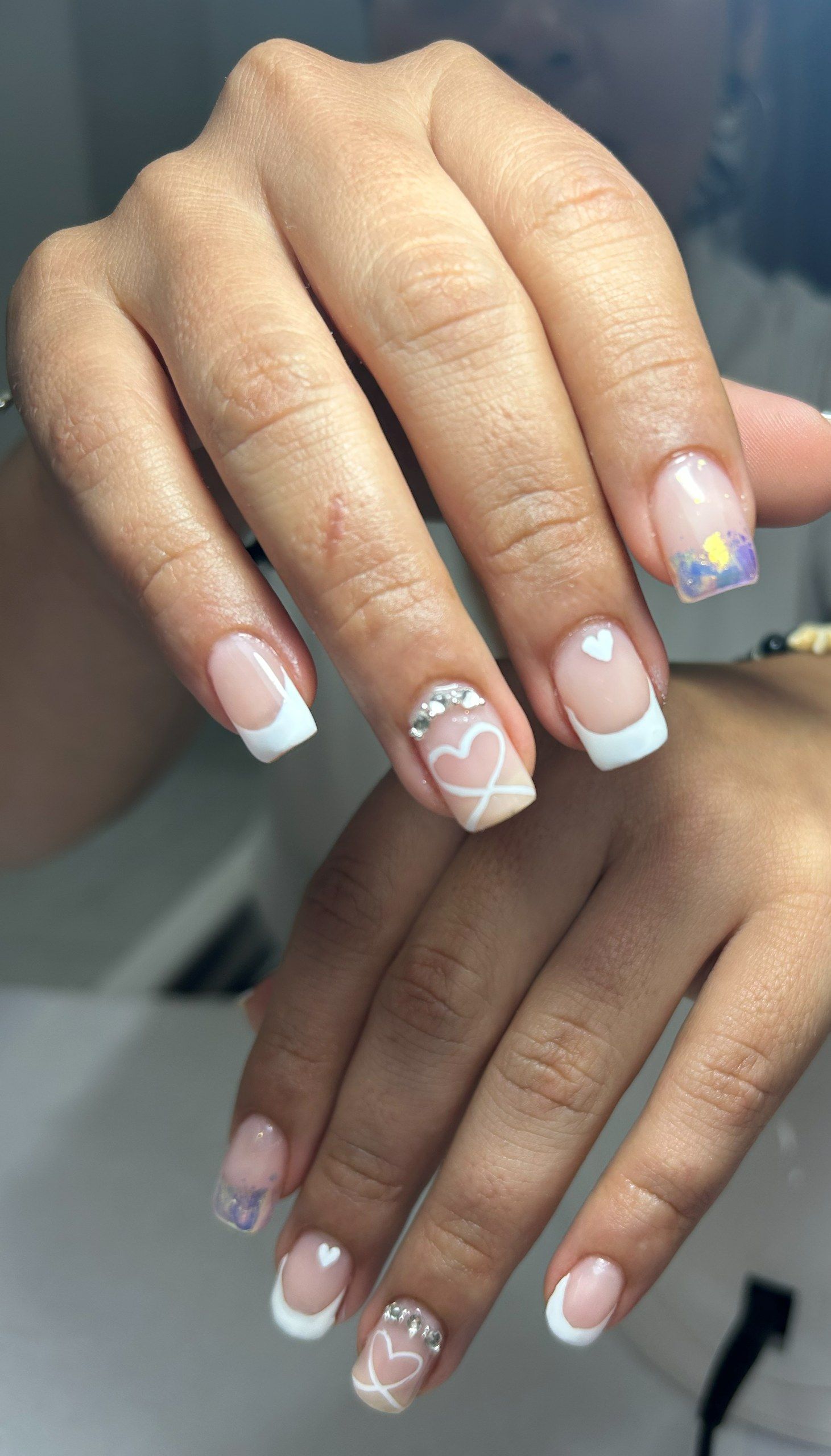 Uñas cuadradas cortas con francesa blanca, corazones delineados, un grupo de cristales y una uña iridiscente