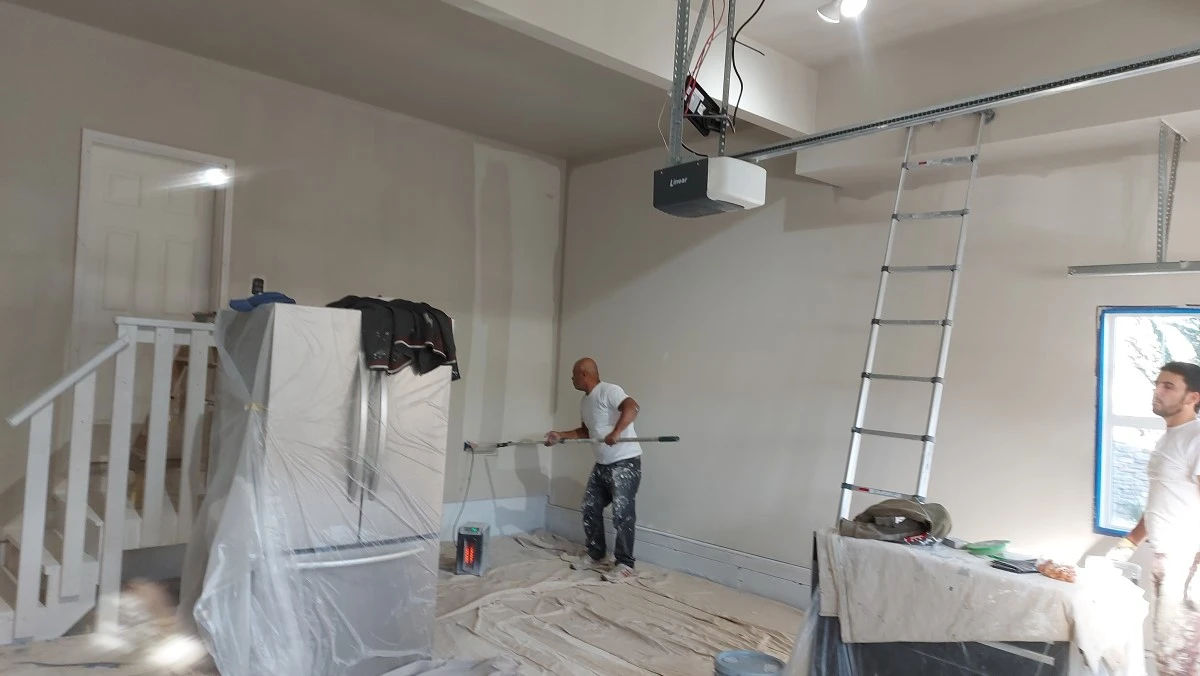 Two painters rolling out a Calgary garage wall, floor sheeted
