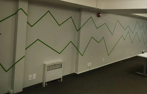 A long office wall carrying its old green zigzag graphic, before repainting
