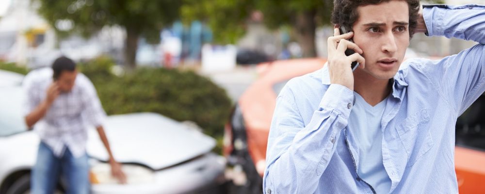 A man having a phone call, on the back you can see a car accident.