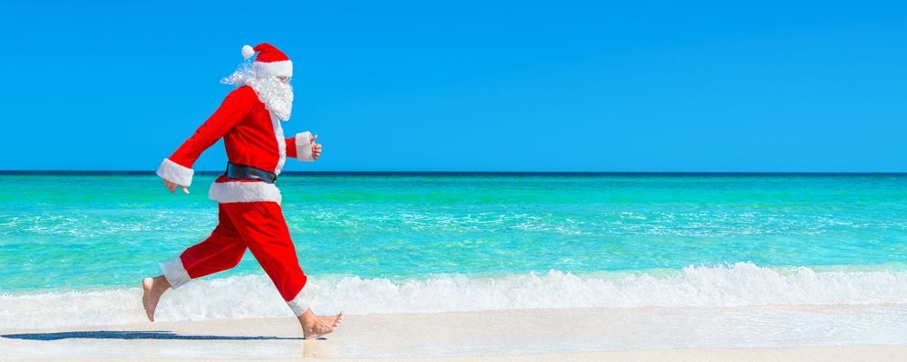 A man dressed up in a Santa Claus costume runs at the beach.