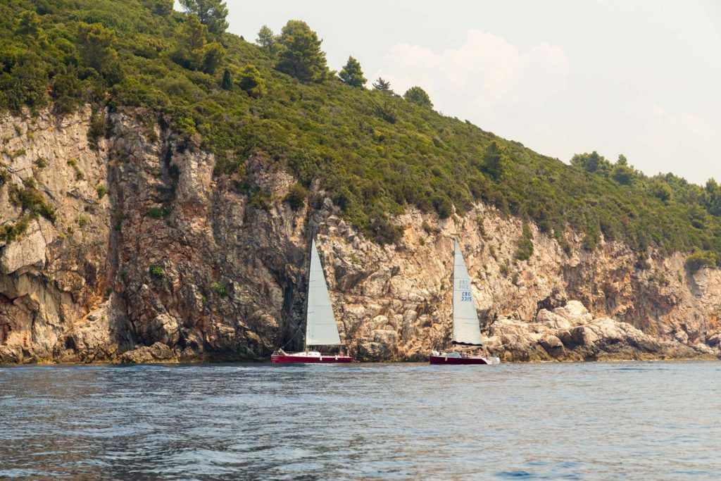 two red sailboats with white sails in front of a cliff sailing in the sea.