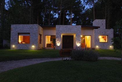 casa moderna con iluminación cálida y fachada de piedra — proyecto Casa Cariló 2006, por Hugo Zawadski Arquitectos, en Cariló