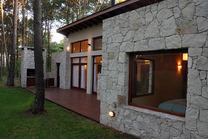 Fachada de casa moderna de piedra con grandes ventanales rodeada de bosque — proyecto Casa Cariló 2006, por Hugo Zawadski Arquitectos, en Cariló