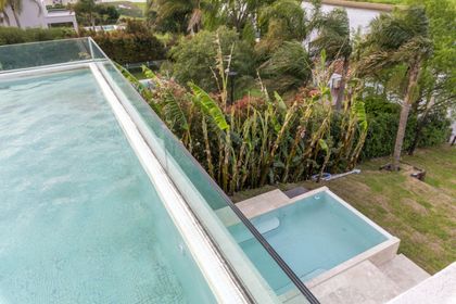 piscina infinita moderna con vegetación exuberante y deck de madera — proyecto Las Caletas, por Arfuso Arquitectos, en Nordelta