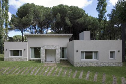 Fachada moderna blanca con base de piedra y detalles en madera — proyecto Casa Cariló 2007, por Hugo Zawadski Arquitectos, en Cariló